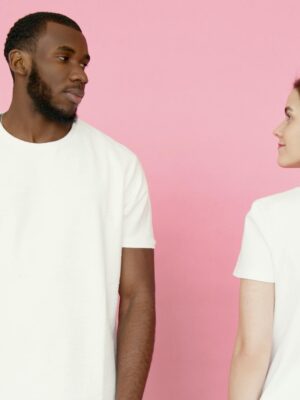 A man and woman in white t-shirts stand against a pink backdrop.