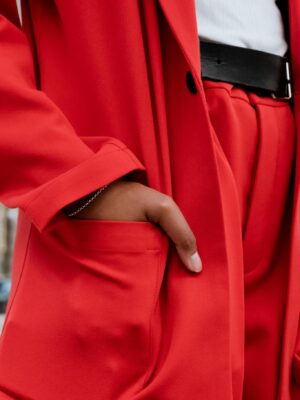 Close-up view of a red suit with a hand in the pocket, showcasing modern fashion style.