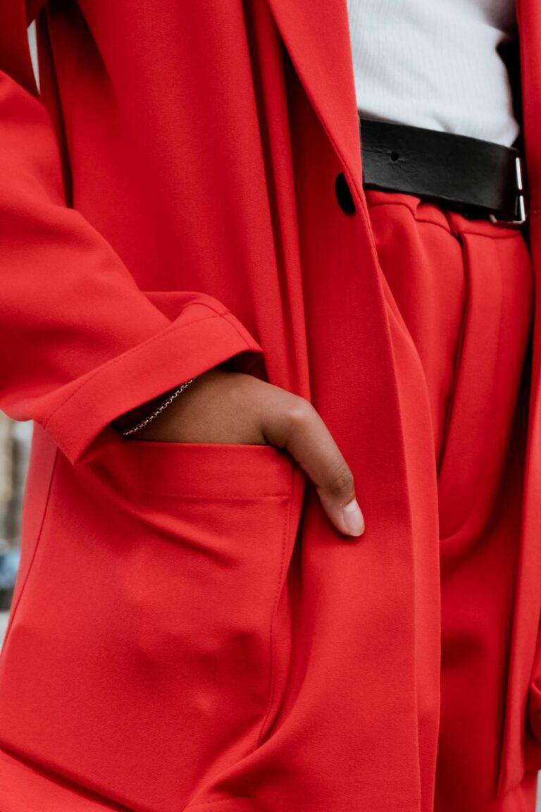 Close-up view of a red suit with a hand in the pocket, showcasing modern fashion style.