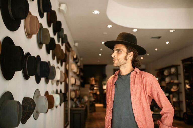 Man in a red shirt browsing fedora hats in a stylish, well-lit hat shop.