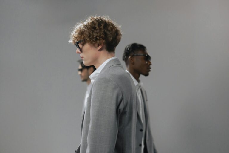 Three stylish men in gray suits and sunglasses, side view with a neutral gray background.